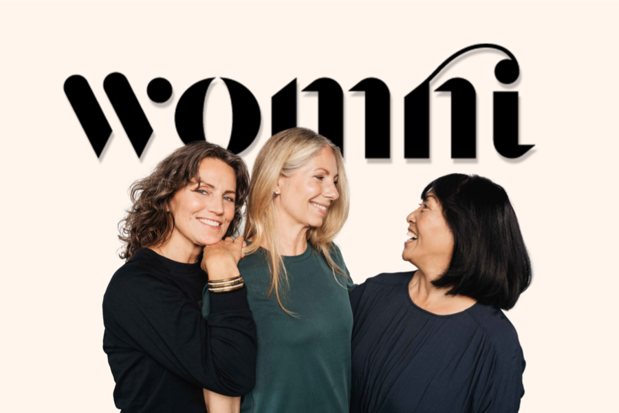 Fyra kvinnor står framför en text där det står Womni