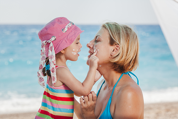 Mamma och dotter smörjer in sig med solskydd på stranden