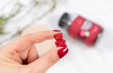 Hand som h&aring;ller i en gummy med vitayummy-produkt i bagrunden.